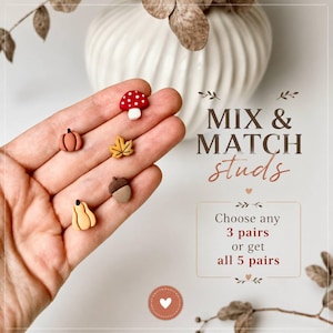Könnte beinhalten: Fünf kleine Ohrstecker in Form eines roten Pilzes mit weißen Punkten, eines orangefarbenen Kürbisses, eines gelben Blattes, einer braunen Eichel und eines hellgelben Kürbisses. Text: MIX & MATCH studs, Choose any 3 pairs or get all 5 pairs.
