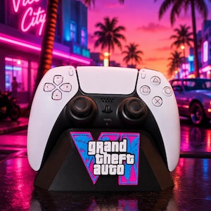 Può includere: Un controller per videogiochi bianco e nero poggiato su un supporto nero con il logo Grand Theft Auto VI in rosa e blu. Il controller presenta pulsanti direzionali standard, due levette analogiche e pulsanti azione con simboli triangolo, cerchio, croce e quadrato.