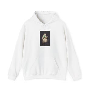 Op de afbeelding: Een witte hoodie met een rechthoekige afbeelding op de borst. De afbeelding toont een spookachtige figuur die een boek en een gloeiend blauw object vasthoudt, met de tekst THE BOOKWRAITH in witte hoofdletters aan de onderkant gedrukt.