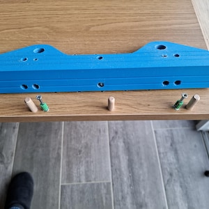 Peut inclure: Un composant de meuble bleu vif avec plusieurs trous et une forme rectangulaire. Plusieurs chevilles en bois et de petites vis sont placées près du composant sur une surface en bois. L'image suggère un assemblage de meubles de bricolage.
