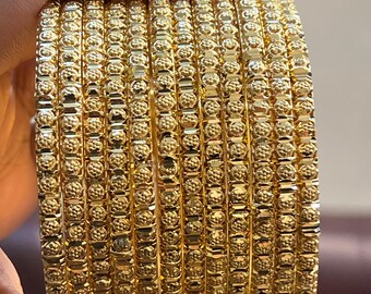 May include: A stack of gold bangles with a textured, dotted pattern. The bangles are held in a hand, showcasing their bright, reflective surface. The jewelry appears to be made of gold.