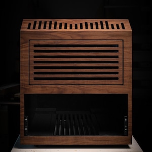 May include: A wooden cabinet with a dark finish, featuring horizontal and vertical vents. The cabinet has a rectangular shape with a glass-fronted lower section. It sits on a white surface against a dark background.