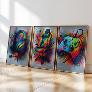 Könnte beinhalten: Drei gerahmte Kunstdrucke mit Gaming-Zubehör. Die Drucke zeigen ein Headset, einen Gaming-Stuhl und einen Controller, jeweils in leuchtenden Regenbogenfarben vor grauem Hintergrund. Das Kunstwerk hat einen dynamischen, spritzartigen Effekt.