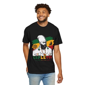 May include: Black t-shirt with a graphic of a man with a beard and white head covering, and the word "CAPLETON" below. The design includes a background of green, yellow, and red stripes, and a lion symbol.