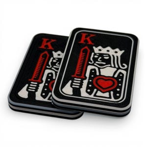 Op de afbeelding: Twee zwarte onderzetters met speelkaarten met een wit en rood ontwerp. Elke onderzetter toont een koning met een zwaard, een rood hart en de letter "K". De onderzetters zijn rechthoekig met afgeronde hoeken.