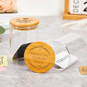 Może przedstawiać: Przezroczysty szklany słoik z bambusową pokrywką i oddzielną bambusową pokrywką z napisem "Reasons why I Love you Kerwin". Słoik jest częściowo wypełniony ciemnym przedmiotem. Kilka małych kartek z tekstem jest rozrzuconych wokół słoika.