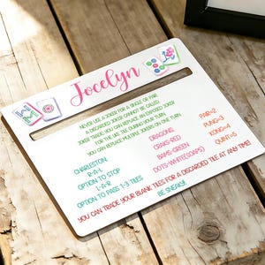 May include: A white Mahjong game rules card with the name "Jocelyn" in pink script. The card includes rules, terms, and scoring information. The card is on a rustic wooden surface.