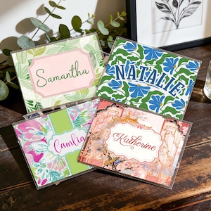 Op de afbeelding: Vier gepersonaliseerde naamkaarten met bloemmotieven. De kaarten tonen namen als "Samantha" en "Natalie" in elegante lettertypen. Het kleurenpalet omvat groen, roze en blauw, met decoratieve randen en patronen.