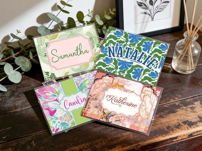 Op de afbeelding: Vier gepersonaliseerde naamkaarten met bloemmotieven. De kaarten tonen namen als "Samantha" en "Natalie" in elegante lettertypen. Het kleurenpalet omvat groen, roze en blauw, met decoratieve randen en patronen.