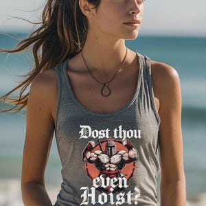 K&ouml;nnte beinhalten: Graues Tanktop mit dem Text "Dost thou even Hoist?" und einer Grafik einer muskul&ouml;sen Figur mit Helm. Das Tanktop ist &auml;rmellos und aus weichem Material. Der Hintergrund ist eine verschwommene Strandszene.