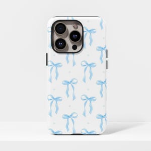 May include: White phone case featuring a pattern of light blue watercolour bows and small dots. The case has a black border and a camera cutout. The bows are tied with long ribbons.