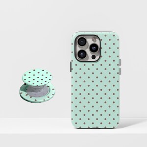 Op de afbeelding: Een mintgroene telefoonhoes en bijpassende telefoonhouder met een bruin stippenpatroon. De telefoonhoes is ontworpen voor een smartphone en de houder is een ronde, inklapbare standaard.
