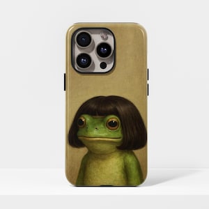 May include: A phone case featuring a whimsical illustration of a green frog with a brown bob haircut. The frog has large, expressive eyes and a serene expression. The case has a tan background and a black camera module.