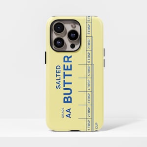 May include: A light yellow phone case featuring a design that mimics a stick of butter. The text "SALTED AA BUTTER" is printed in blue, along with a measurement guide in tablespoons and a cup measurement.