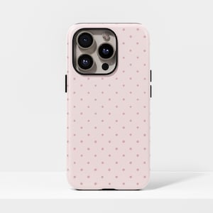 Può includere: Una custodia per telefono rosa con un motivo ripetuto di piccoli pois rosa scuro. La custodia ha un anello per fotocamera nero e pulsanti laterali neri. La custodia del telefono è su una superficie bianca.