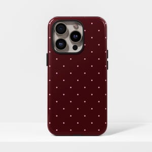 May include: A glossy burgundy phone case featuring a pattern of small, evenly spaced pink polka dots. The case has a camera cutout with three lenses and a flash.