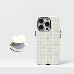 May include: A phone case and matching phone grip featuring a light green gingham pattern with small purple floral accents. The phone case is designed to fit a smartphone, and the grip is a circular shape.