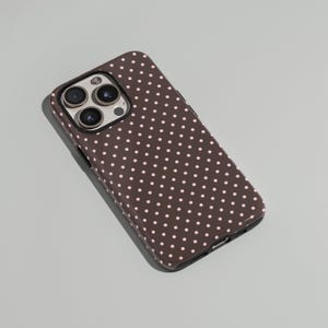 May include: A brown phone case with a repeating pattern of small, light pink polka dots. The case has a glossy finish and a camera cutout with three lenses.