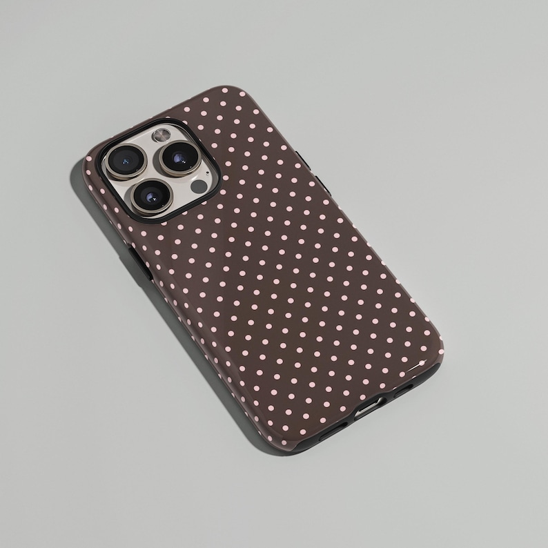 May include: A brown phone case with a repeating pattern of small, light pink polka dots. The case has a glossy finish and a camera cutout with three lenses.