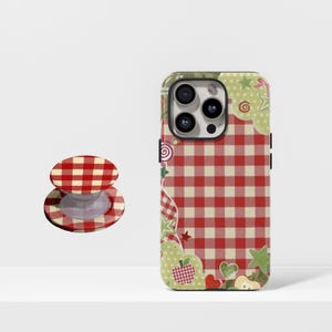 May include: A red and white checkered phone case and matching pop socket. The case has a gingham pattern with decorative green and red apple, star, and heart accents. The pop socket is round with a red and white checkered design.