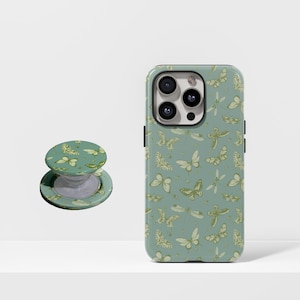 Puede incluir: Una funda para teléfono móvil y un soporte para teléfono con un patrón a juego de mariposas y libélulas en tonos verdes y beige. La funda está a la derecha y el soporte a la izquierda.