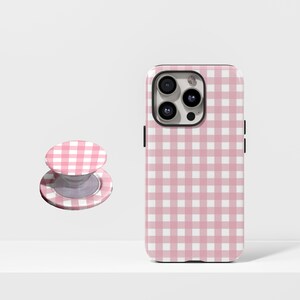 May include: A pink and white gingham patterned phone case and matching phone grip. The phone case is designed to fit a smartphone, and the grip is a round, collapsible stand for the back of the phone.