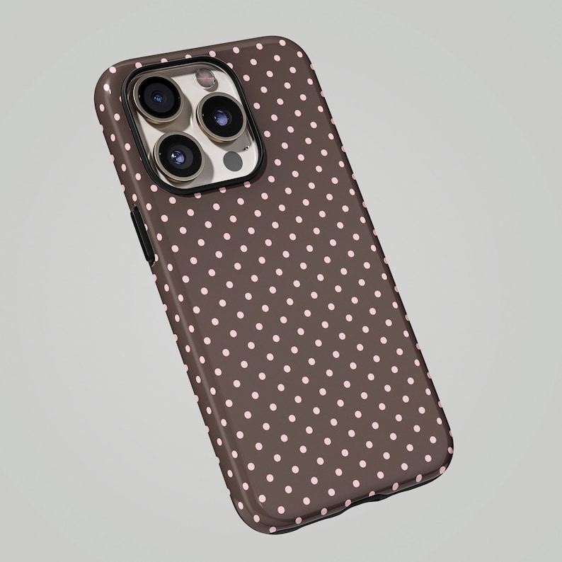 May include: A brown phone case with a pattern of small, evenly spaced pink polka dots. The case has a glossy finish and a camera cutout. The phone case is designed to fit a smartphone.