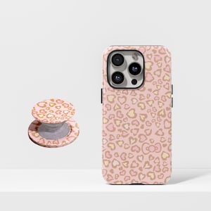 May include: A pink phone case and matching phone grip featuring a heart-shaped leopard print design. The case is designed to fit a smartphone, and the grip is a round, pop-out style accessory.