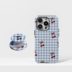 May include: A phone case and a phone grip with a blue and white gingham pattern and a cherry design. The phone case is on the right, and the phone grip is on the left. The cherries are red with green stems.
