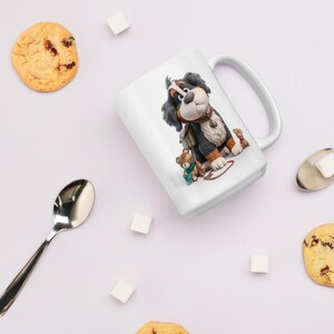 May include: White ceramic mug featuring a cartoon Bernese Mountain Dog with a teddy bear. The dog is black, brown, and white, wearing a brown collar. A spoon, sugar cubes, and cookies are also visible.