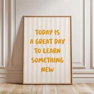 May include: Framed print with a light brown wooden frame. The artwork features a striped background in cream and light orange. The text in the center reads "TODAY IS A GREAT DAY TO LEARN SOMETHING NEW" in orange lettering.
