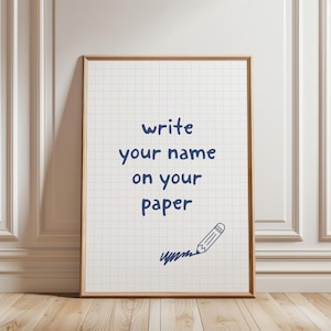 May include: A framed print with a grid pattern background and the text "write your name on your paper" in navy blue. A pencil drawing is in the lower right corner. The frame is a light brown color.