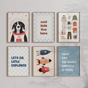 Puede incluir: Seis láminas enmarcadas con temática espacial. Una lámina presenta un perro con un casco de astronauta. Otras láminas tienen cohetes y citas inspiradoras: "cool kids live here", "Let's go, little explorer" y "Shine like the whole universe is yours."