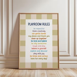 May include: A framed print with a beige and green checked border. The white interior features the words "PLAYROOM RULES" in navy blue, followed by a list of positive affirmations in various colours, including "be respectful" and "have fun every day!"