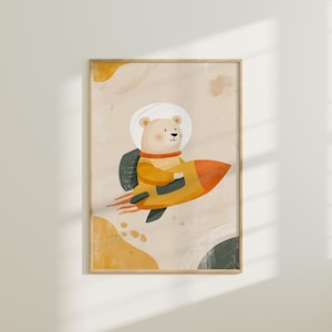 May include: A framed art print depicting a cartoon bear in a spacesuit, soaring on a yellow and orange rocket. The bear is set against a beige backdrop with abstract yellow and green shapes. The artwork has a whimsical, childlike aesthetic.