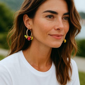 May include: Gold hoop earrings with colorful fruit charms. The earrings feature red, yellow, and green accents, creating a vibrant and playful design. The hoops are adorned with small, sparkling embellishments, adding a touch of elegance to the fun fruit theme.