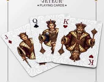 Puede incluir: Tres cartas de la baraja Jeteur Playing Cards, que muestran la sota de diamantes, la reina de tréboles y el rey de corazones. Cada carta presenta una ilustración detallada y ornamentada de una figura real con vestimenta dorada y roja sobre fondo blanco.