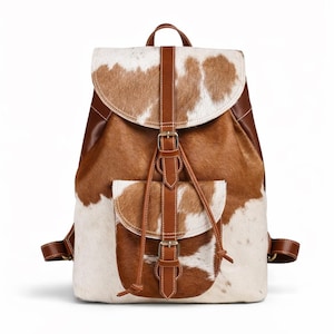 May include: A cowhide backpack with a brown and white pattern. The bag features brown leather accents, including straps, a flap closure, and a front pocket. The backpack has a top handle and adjustable shoulder straps.