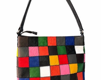 Puede incluir: Un bolso de hombro rectangular con un diseño de patchwork multicolor compuesto por paneles cuadrados en rojo, azul, verde, amarillo, rosa, blanco, negro, marrón y gris. El bolso incluye una correa de hombro negra y cierre de cremallera.