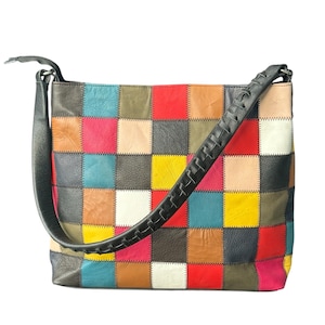 Puede incluir: Un bolso de hombro de patchwork multicolor con una correa trenzada negra. El bolso está hecho de cuadrados de cuero en varios colores, incluyendo rojo, azul, amarillo y verde. El bolso tiene forma rectangular.