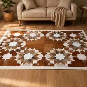 May include: A rectangular area rug featuring a geometric star pattern composed of brown, white, and gray cowhide patches. The rug has a solid white border and a repeating symmetrical design of interlocking star shapes across the entire surface.