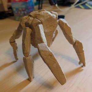 May include: A tan-colored, multi-legged figurine constructed from angular, rock-like segments. The creature features a central, bulky body mass supported by several articulated, limb-like appendages that extend outward, mimicking a stone-based entity.