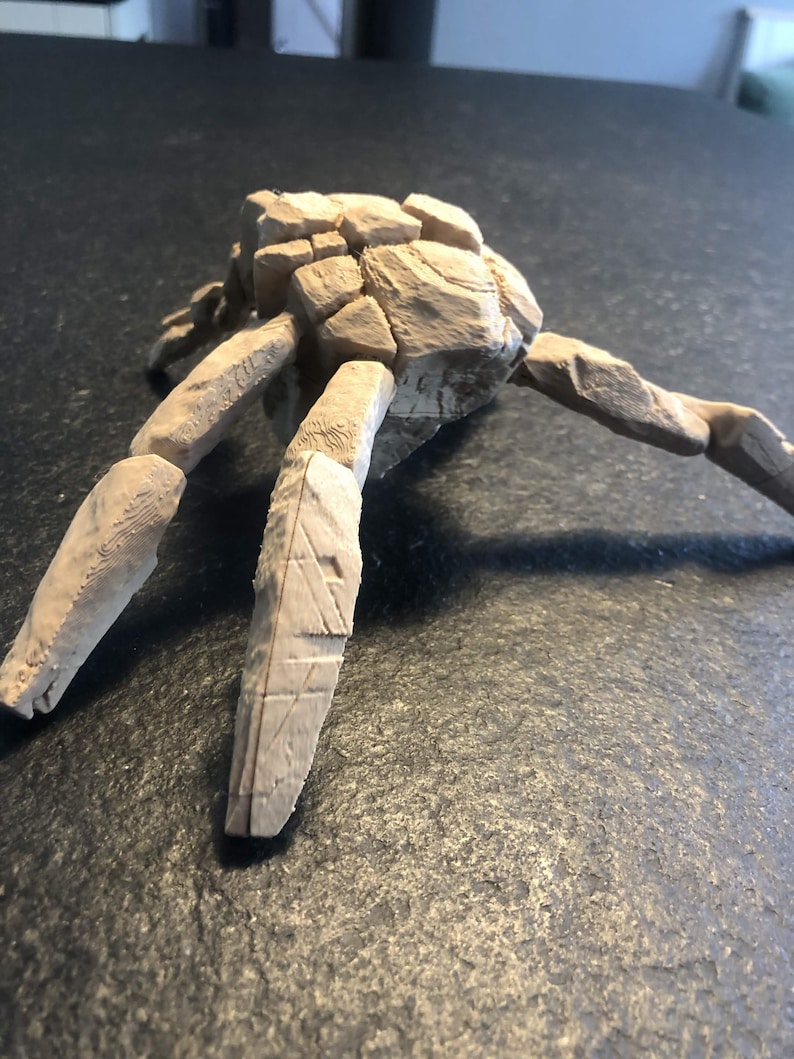 May include: A light beige, multi-legged sculpture with a textured, cracked surface resembling assembled stone fragments. The object features a central cluster of blocky, irregular shapes with several elongated, segmented limbs extending outward.