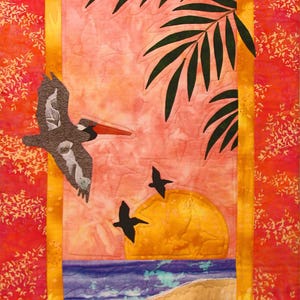 May include: A fabric artwork showing a sunset scene with a pelican in flight. The piece uses a vibrant palette of orange, pink, yellow, and blue. Palm fronds and two smaller birds are also included in the design.