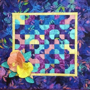 May include: A handmade quilt with a floral design. The quilt features a central square with a patchwork pattern in shades of blue, purple, pink, and yellow, framed by a yellow border. The background is a dark blue floral print, and it has appliqued flowers.