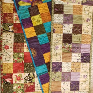 May include: Three colourful, handmade quilted table runners. Each runner features a patchwork design with squares of various fabrics in shades of red, gold, green, purple, and blue. The runners have decorative fan-shaped ends.
