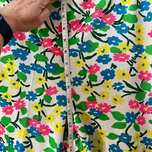 Puede incluir: Tela blanca con un colorido estampado floral de flores rosas, azules y amarillas con hojas verdes. Una cinta m&eacute;trica muestra una longitud de aproximadamente 40 cm. La tela es adecuada para ropa o decoraci&oacute;n del hogar.