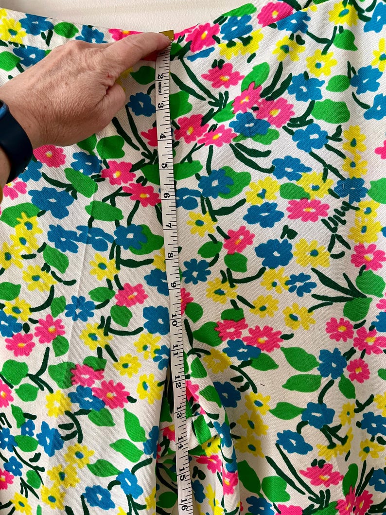 Puede incluir: Tela blanca con un colorido estampado floral de flores rosas, azules y amarillas con hojas verdes. Una cinta m&eacute;trica muestra una longitud de aproximadamente 40 cm. La tela es adecuada para ropa o decoraci&oacute;n del hogar.