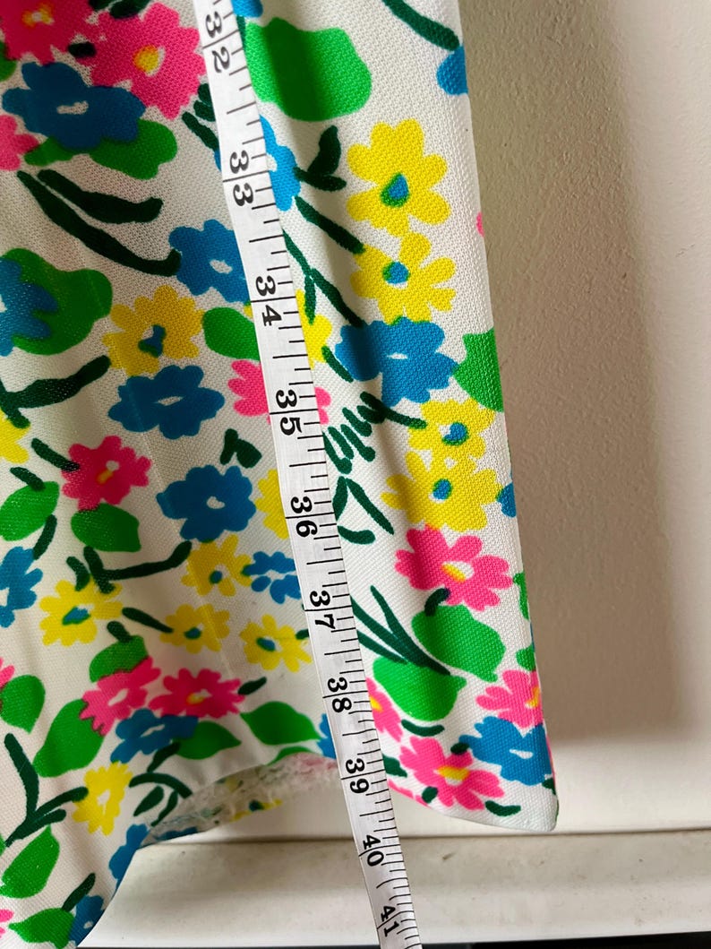 Puede incluir: Tela blanca con un vibrante estampado floral en rosa, amarillo y azul. Una cinta m&eacute;trica muestra medidas de 81 a 104 cm. El dise&ntilde;o se completa con hojas y tallos verdes.