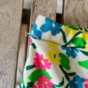Puede incluir: Primer plano de una tela con estampado floral. La tela presenta un fondo blanco con flores rosas, amarillas y azules brillantes, junto con hojas verdes. La tela es ligeramente texturizada y parece ser parte de una prenda.